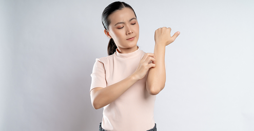 Woman with a calm expression rubs her forearm against a light background.